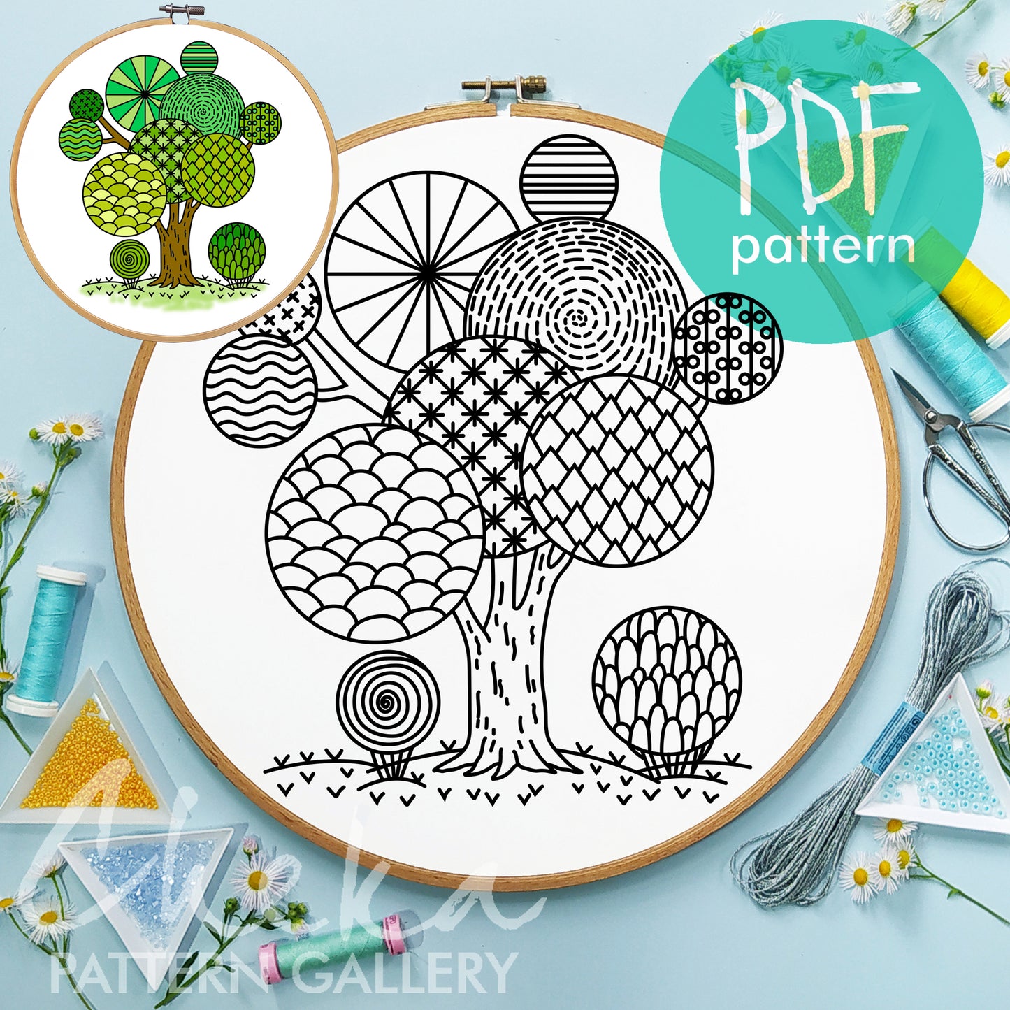 Embroidery hoop with a tree pattern, surrounded by sewing supplies on a light blue background.