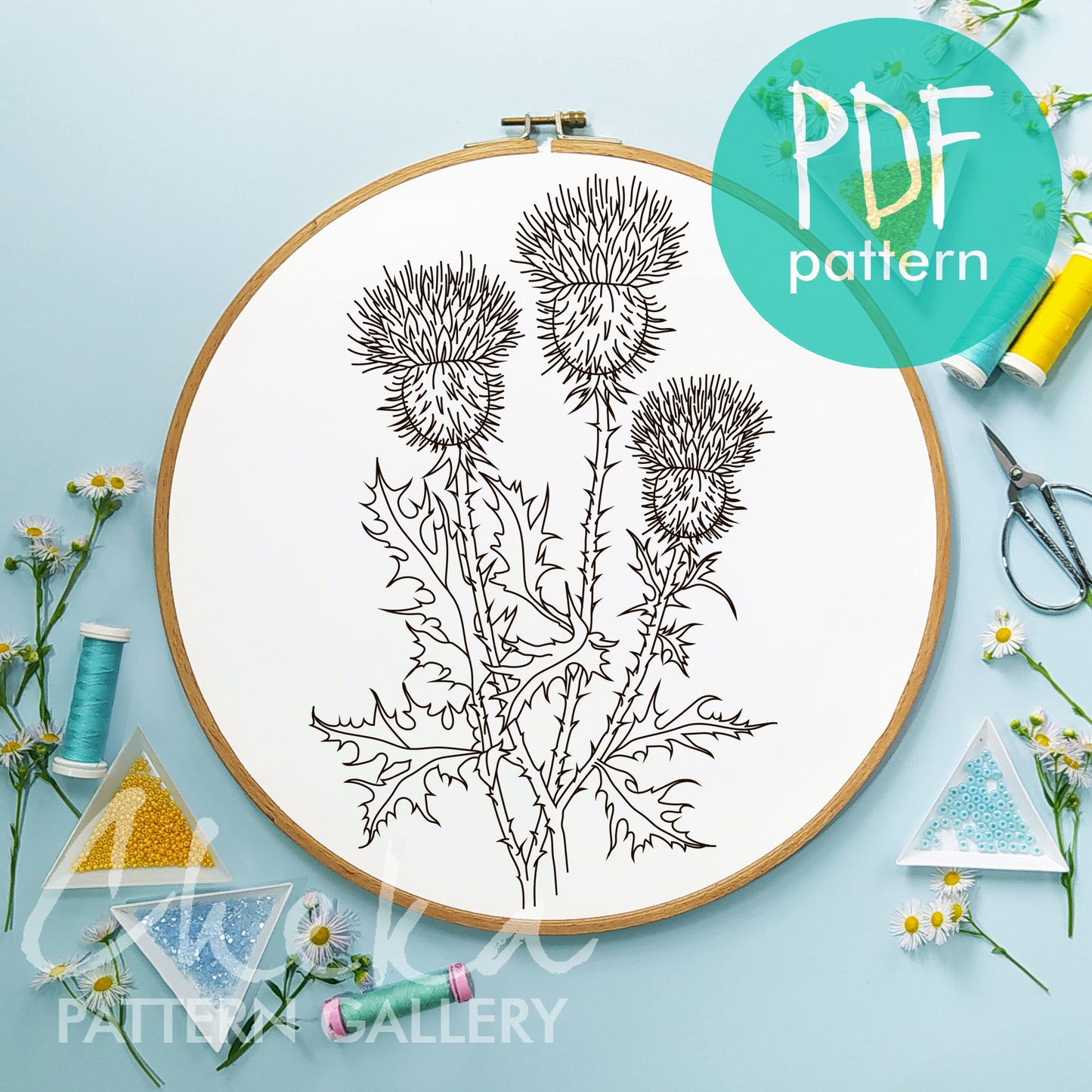Embroidery hoop with thistle pattern on a light blue background, featuring sewing supplies.