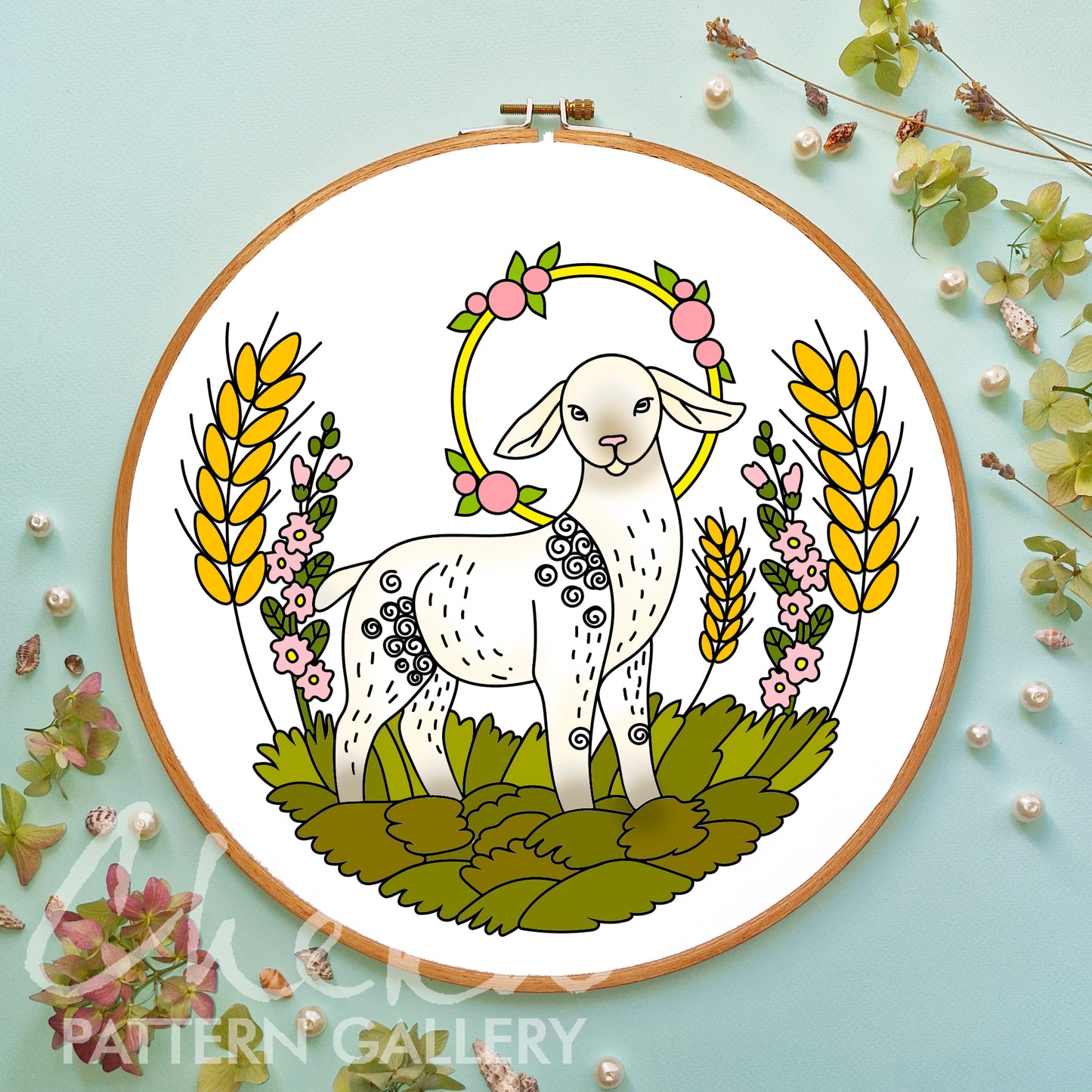 Embroidery hoop with a white lamb design surrounded by flowers and leaves on a light blue background.