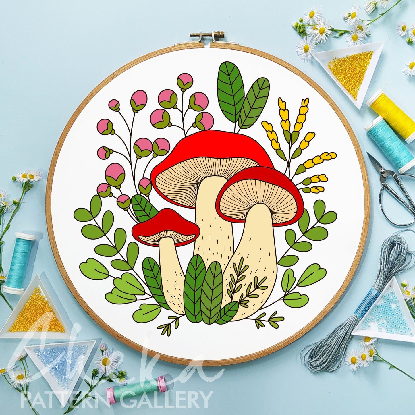 Embroidery hoop with a colorful mushroom design on a light blue background with embroidery supplies.