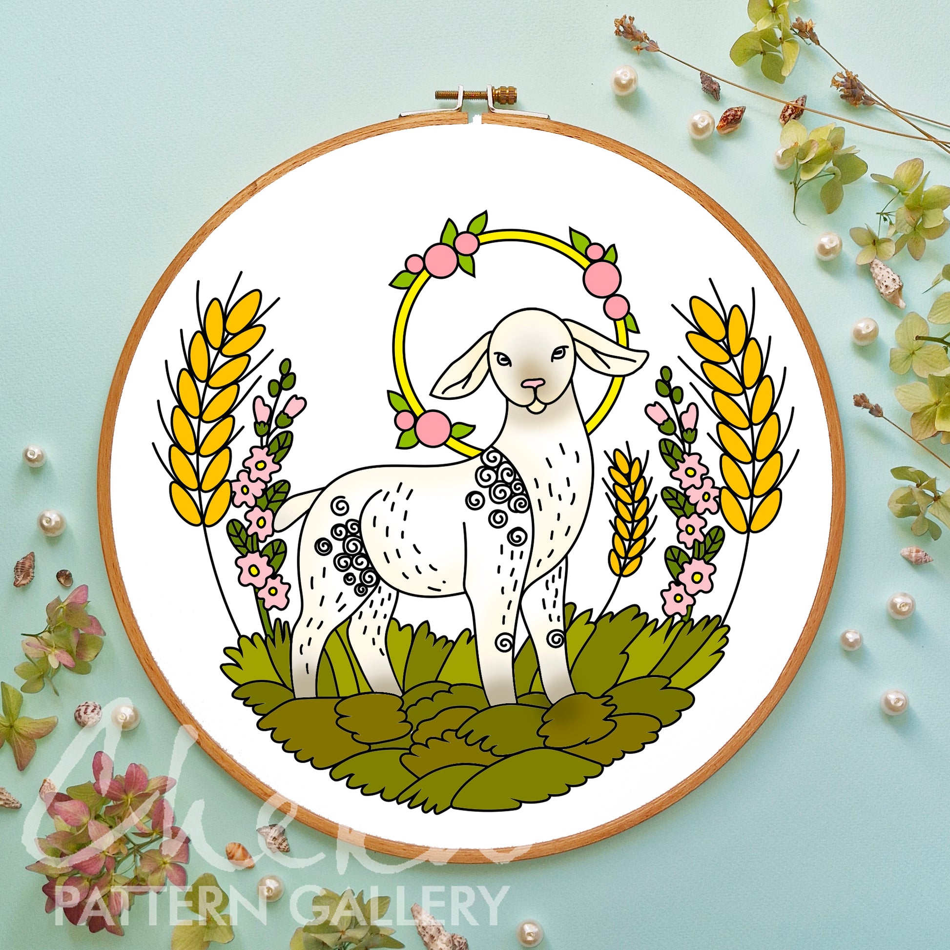 Embroidery hoop with a white lamb design surrounded by flowers and leaves on a light blue background.