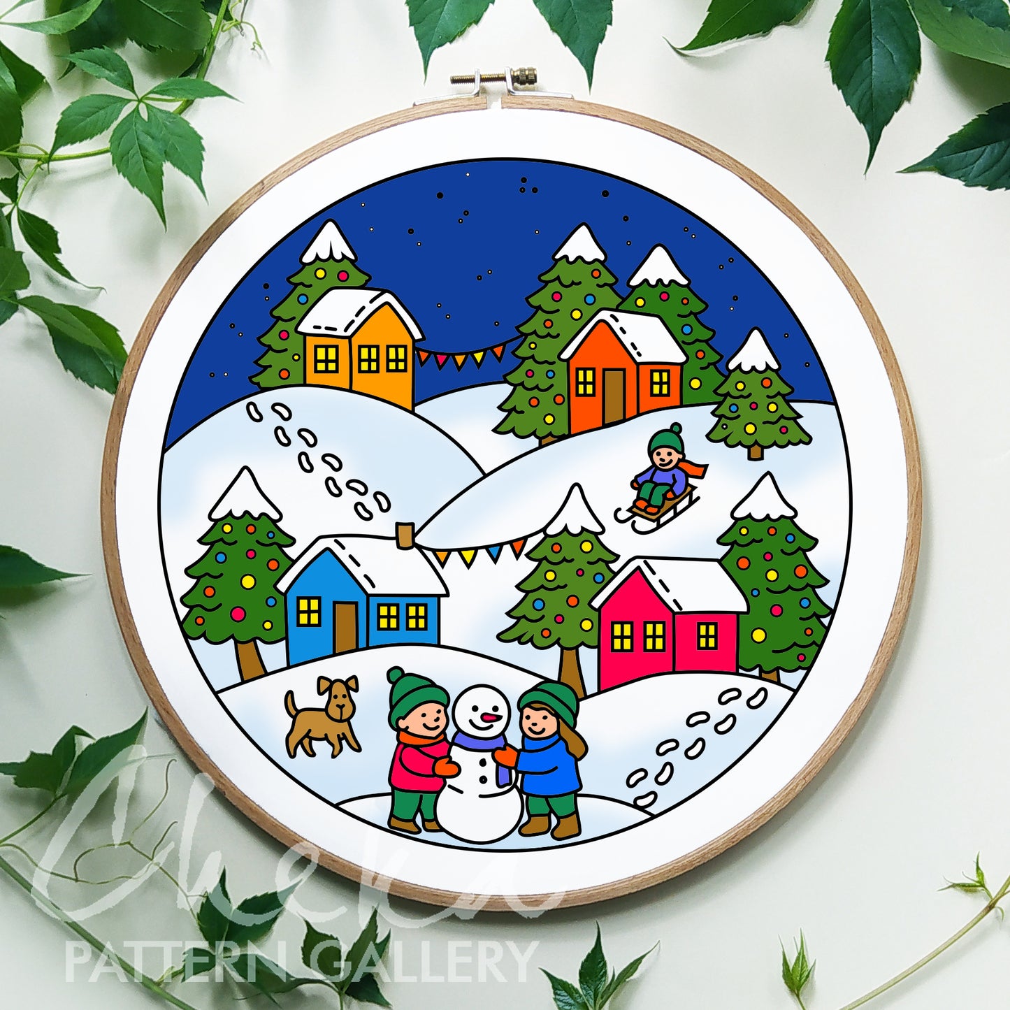 Embroidery hoop with a winter scene featuring houses, trees, and people on a white background.
