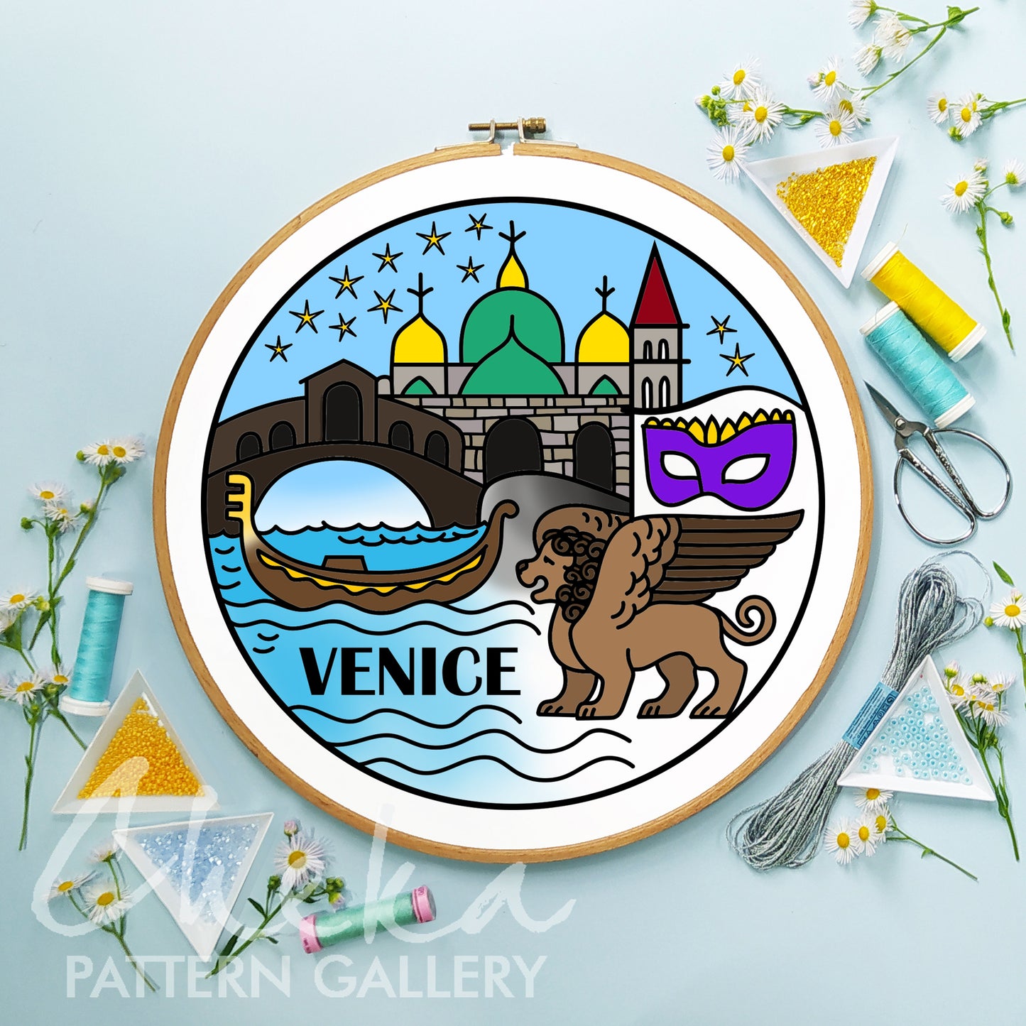Embroidery hoop with Venice-themed design on a light blue background with sewing supplies.