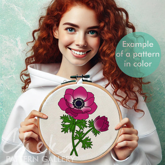 Woman holding a floral embroidery hoop with a pink flower design against a light green background.
