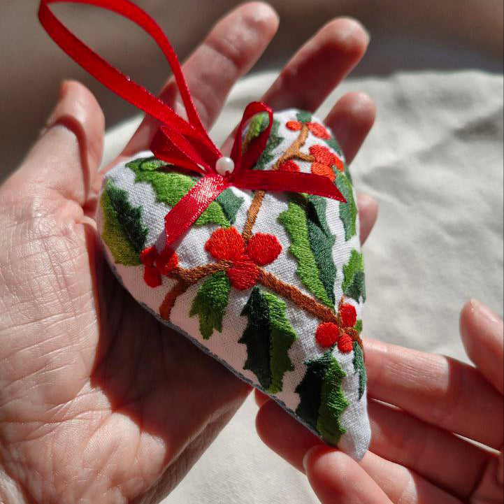 Heart-shaped embroidered ornament with red ribbon held in a hand