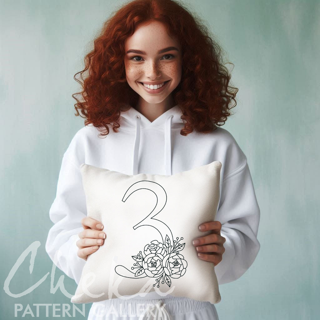 Woman holding a pillow with a floral number three design against a light green background